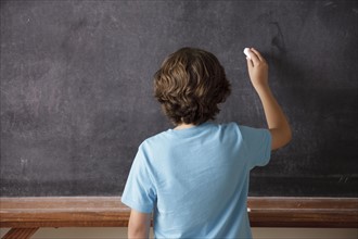Rear view of schoolboy (10-11) writing on blackboard. 
Photo : Rob Lewine
