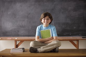 Portrait of schoolboy (10-11) cross-legged sitting in front of blackboard. 
Photo: Rob Lewine