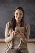 Portrait of teacher in classroom holding digital tablet. 
Photo : Rob Lewine