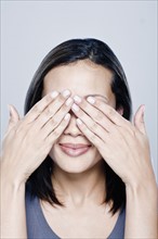 Portrait of young woman with hands covering eyes, studio shot. 
Photo : Rob Lewine