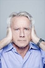 Portrait of senior man covering his ears, studio shot. 
Photo: Rob Lewine