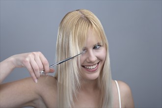 Woman cutting bangs, studio shot. 
Photo : Mark de Leeuw