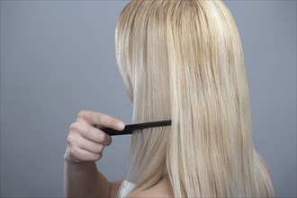 Woman combing hair, studio shot. 
Photo : Mark de Leeuw