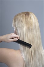 Woman combing hair, studio shot. 
Photo : Mark de Leeuw