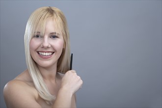 Portrait of young woman combing hair, studio shot. 
Photo: Mark de Leeuw