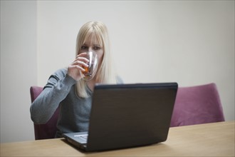 Netherlands, Goirle, Young woman relaxing in front of laptop and drinking tea. 
Photo: Mark de