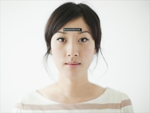 Portrait of young woman with word 'educated' on forehead, studio shot. 
Photo: Jessica Peterson
