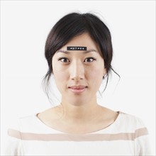 Portrait of young woman with word 'mother' on forehead, studio shot. 
Photo : Jessica Peterson