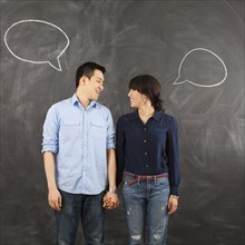 Young couple with speech bubbles on chalkboard, studio shot. 
Photo : Jessica Peterson