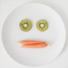 Fruit and vegetable face on plate, studio shot. 
Photo : Jessica Peterson
