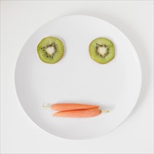 Fruit and vegetable face on plate, studio shot. 
Photo: Jessica Peterson