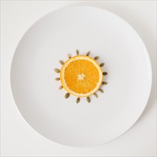 Slice of orange and seeds on plate, studio shot. 
Photo : Jessica Peterson