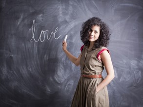 Young teacher posing against blackboard with word love written on it. 
Photo : Jessica Peterson