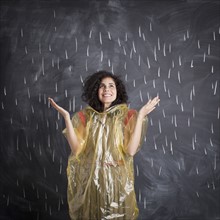 Young teacher wearing raincoat posing against blackboard with V marks imitating rain. 
Photo: