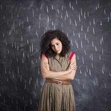 Young depressed teacher posing against blackboard with V marks imitating rain. 
Photo : Jessica