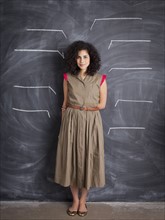Young teacher posing against blackboard with blank lines written in chalk. 
Photo: Jessica