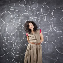 Young teacher posing against blackboard with bubbles written in chalk. 
Photo : Jessica Peterson