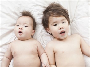 Mixed race siblings (2-5 months, 2-3) lying in bed side by side. 
Photo : Jessica Peterson