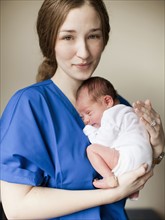 Portrait of young female nurse holding baby boy (2-5 months). 
Photo : Jessica Peterson