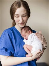 Portrait of young female nurse holding baby boy (2-5 months). 
Photo : Jessica Peterson