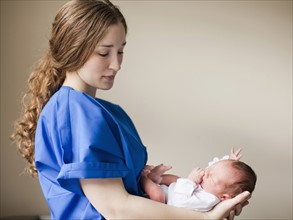 Portrait of young female nurse holding baby boy (2-5 months). 
Photo : Jessica Peterson