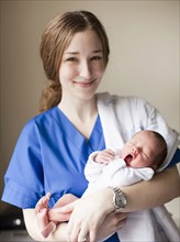 Portrait of young female nurse holding baby boy (2-5 months). 
Photo : Jessica Peterson