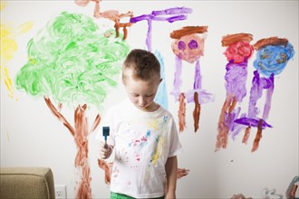 Toddler boy (2-3) standing in front of painted wall with guilt expression on his face. 
Photo: