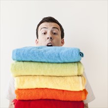Overburdened young man holding stack of multi-coloured towels. 
Photo : Jessica Peterson