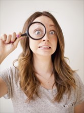 Young woman making a face while holding magnifying glass. 
Photo : Jessica Peterson