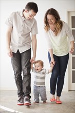 Young couple assisting baby boy (6-11 months) in first steps. 
Photo: Jessica Peterson