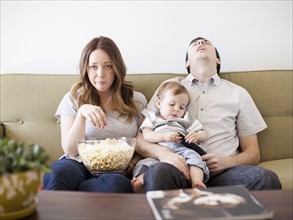 Young couple with baby boy (6-11 months) watching TV. 
Photo : Jessica Peterson