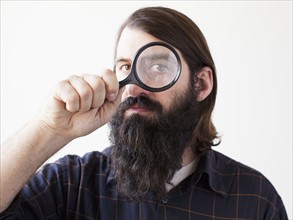 Bearded young man looking through magnifying glass. 
Photo : Jessica Peterson