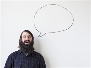 Bearded young man standing next to speech bubble on white background. 
Photo : Jessica Peterson