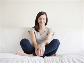 Happy young woman sitting on bed. 
Photo: Jessica Peterson