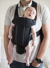 Young father holding baby daughter (2-3 months) in carrycot. 
Photo : Jessica Peterson