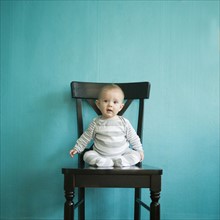 Toddler boy (2-3) sitting on tall chair on blue background. 
Photo : Jessica Peterson