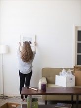 Young woman hanging picture on freshly painted wall. 
Photo: Jessica Peterson