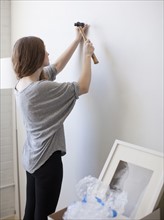 Young woman hanging picture on freshly painted wall. 
Photo: Jessica Peterson