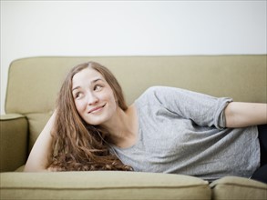 Happy young woman reclining on sofa. 
Photo : Jessica Peterson