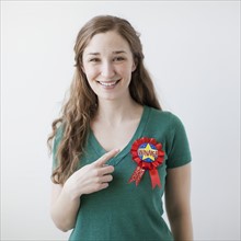 Studio shot of happy young woman showing winner badge. 
Photo : Jessica Peterson