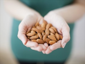 Studio shot of woman showing handful of almonds. 
Photo : Jessica Peterson