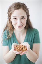 Studio shot of woman showing handful of almonds. 
Photo : Jessica Peterson