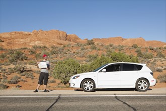 USA, Utah, Moab, Man standing beside car reading map. 
Photo : Jessica Peterson
