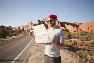 USA, Utah, Moab, Man standing on roadside, reading map. 
Photo : Jessica Peterson