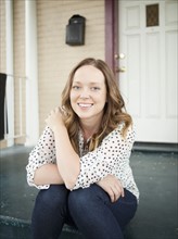 Portrait of happy young woman sitting on porch. 
Photo : Jessica Peterson