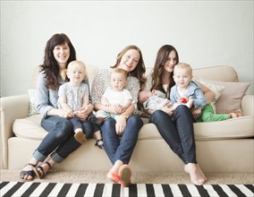 Three young mothers with toddler girl (2-3) and tow baby boys (2-5 months, 6-11 months) posing for