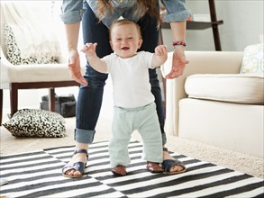 Young mother assisting baby boy (6-11 months) in his first steps. 
Photo: Jessica Peterson