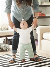 Young mother assisting baby boy (6-11 months) in his first steps. 
Photo: Jessica Peterson