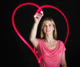 Woman drawing heart on black background.