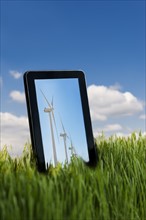 Tablet PC in grass with wind turbines on screen.